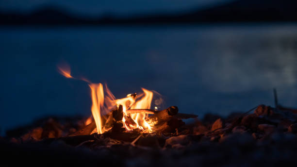 istock Small campfire with gentle flames beside a lake during blur hour. 1417962567