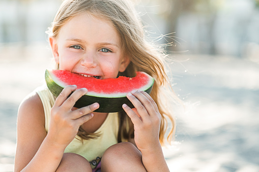 Portrait happy smile child little adorable girl eat piece of juice watermelon fruit on beach. summertime and picnic outdoors. Banner, copy space, place fot text, isolated. Nature background