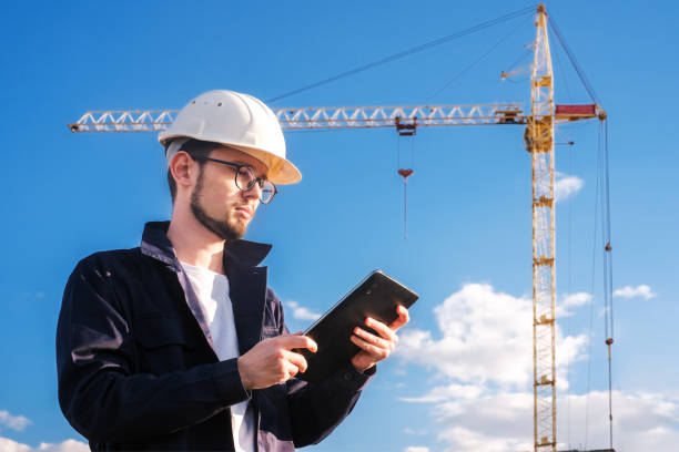 istock a builder looks at a tablet against the background of a house under construction with a crane 1417962911