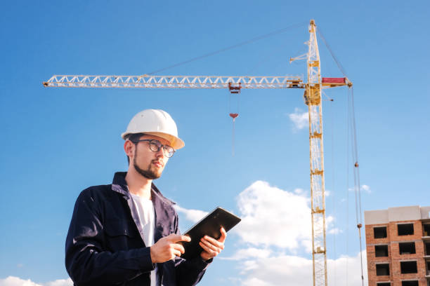 istock a builder looks at a tablet against the background of a house under construction with a crane 1417962921