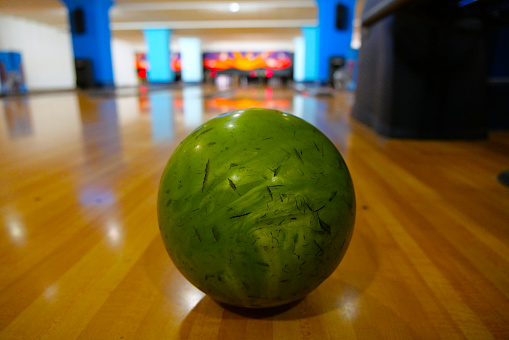 A green bowling ball in on the wooden floor of a bowling facility.