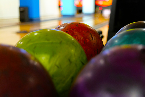 Green, red, blue, purple and black bowling balls in on the wooden floor of a bowling facility.