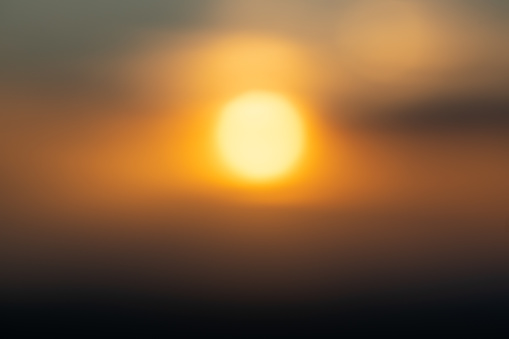 Blurred defocused background of sunset at the sea - Abstract bokeh of sun going down through the clouds over the horizon - Emotional concept of deep connection with nature wonders