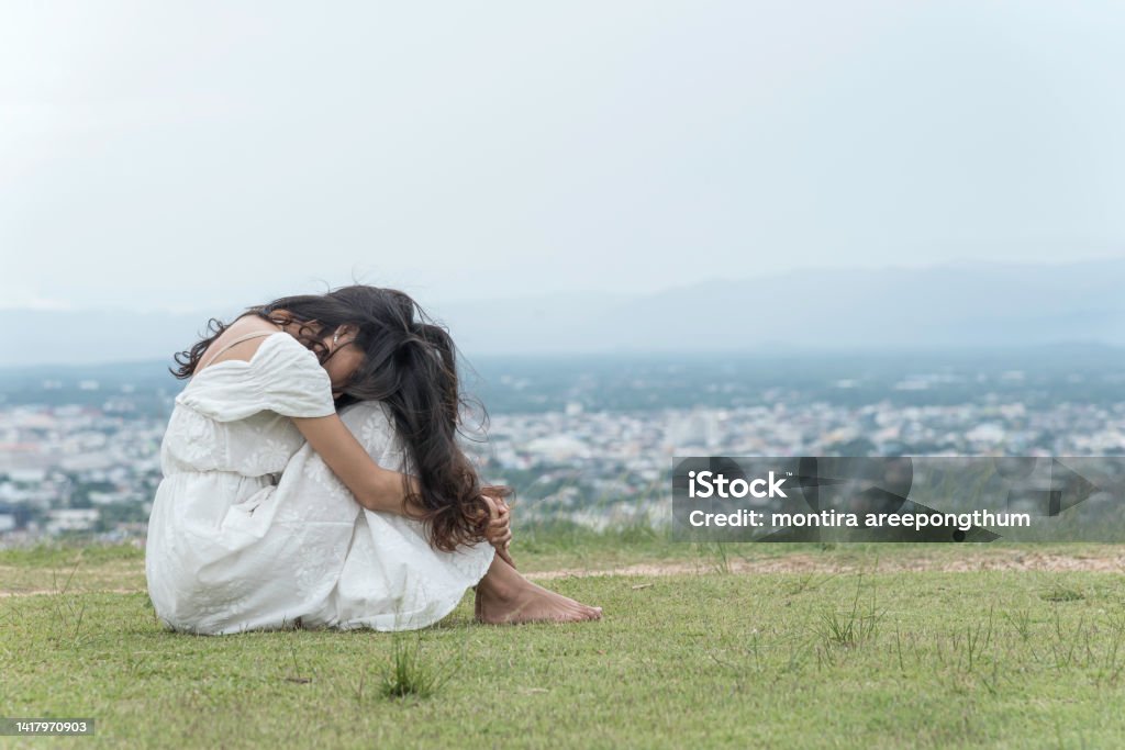 woman sit facing side face down knee on grass at top mountian sky ,city and nature view background. feel sad and depress.. woman sit facing side face down knee on grass at top mountian sky ,city and nature view background. feel sad and depress. 20-24 Years Stock Photo