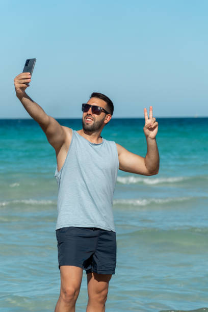 istock Young man with beard and sunglasses taking a selfie with his smartphone on the beach on a sunny day. 1417973872
