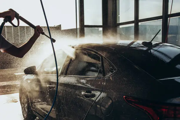 Photo of A man washes his car at a self-service car wash using a hose with pressurized water