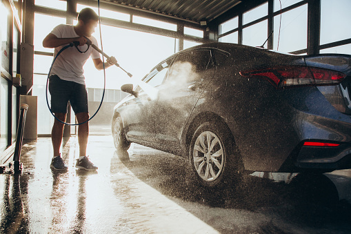 A man washes his car at a self-service car wash using a hose with pressurized water.