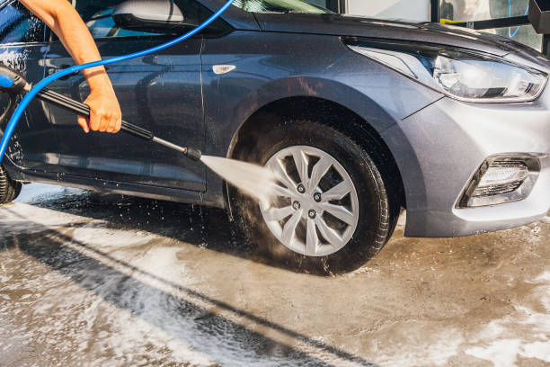 мужчина моет колеса на своем автомобиле на автомойке самообслуживания с помощью шланга с водой под давлением - hose of a high pressure стоковые фото и изображения