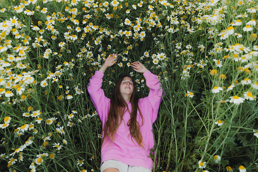 High Angle view of happy female with long hair relaxing on the beautiful field with daisy flowers in bloom in Turkey during sunset
