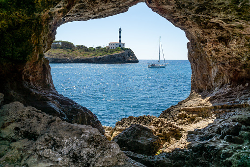 Inside a cave overlooking the sea and a red and white lighthouse with a ship sailing