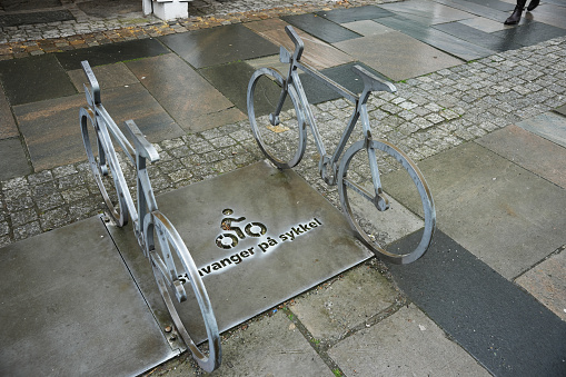 Bike rack in Stavanger, Norway.  It has been raining heavily and the ground is wet.  The bike racks feature a wrought iron bike and metal plates.