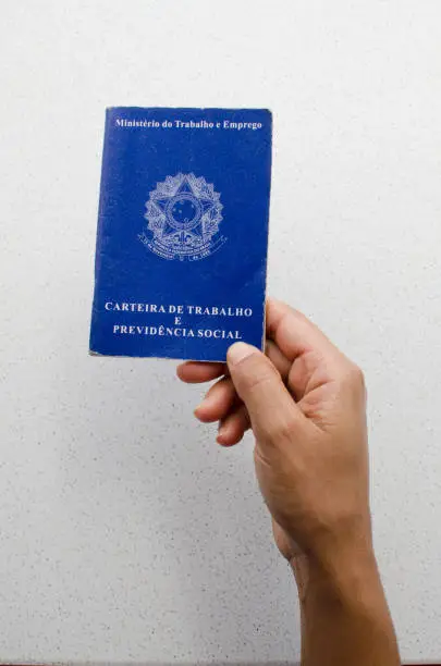 Translation: 'Federative Republic of Brazil, Ministry of Labour'. Brazilian notebook. Concept of FGTS, unemployment, salary and Brazilian economy. Hand holding (Carteira de Trabalho brasileira).