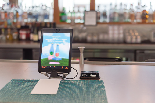 Tablet with swipe magnetic credit card reader to order food and drink at airport bar restaurant in Texas, USA. Table placemats with napkin ready for customer to dine in, social distancing concept