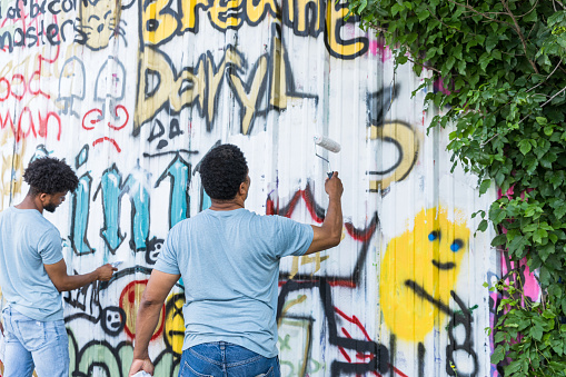 Street artist painting colored graffiti on public space wall - Modern art concept of urban guy performing and preparing live murales paint with yellow aerosol color spray - Cloudy afternoon filter