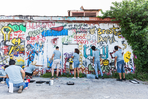 A rear view photo of a diverse group of people painting over the graffiti at their local park.