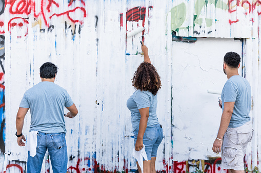 A rear view photo of three volunteers as they paint over graffiti.