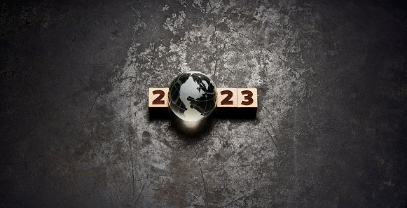Panoramic stich photography of wooden cubes and a glass globe on old metal. The globe is placed in the center of the image and is showing North America. The wooden cubes are showing the date 2023. Native image size: 10390 x 5315