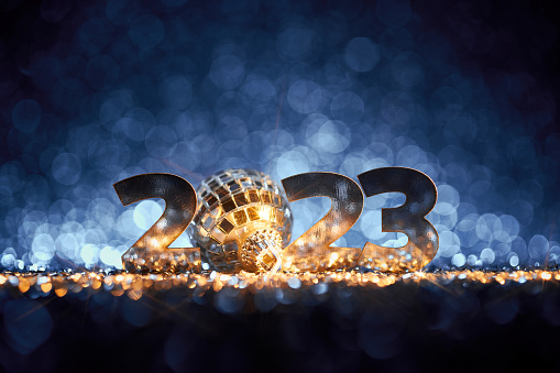 Abstract Christmas / New Year 2023 background. Metallic serif numbers and a disco ball Christmas ornament on shiny stars, glitter and defocused lights in a yellow blue contrast. Native image size: 7952x5304