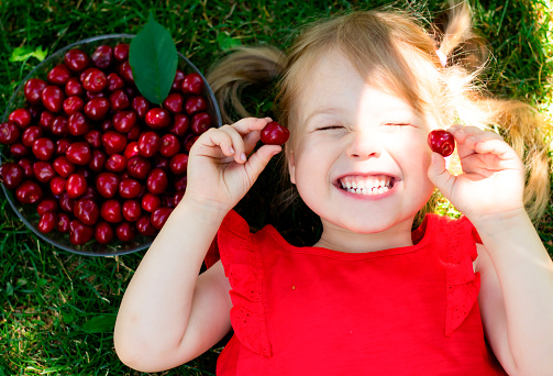 Happy child's face in the rays of the sun with two berries of cherries on her hands
