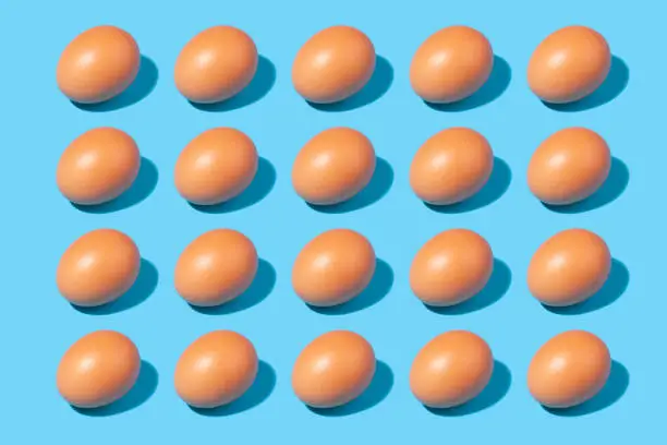 Creative pattern of brown eggs - conceptual background - chicken eggs in a row on a blue background