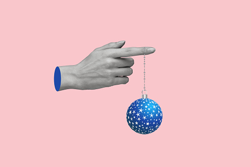 Contemporary art collage of female hand holding christmas ball. Concept of Christmas, New Year, holiday, celebration, and winter. Copy space on a pink background.