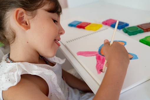 Little child girl painting with her watercolors with a brush. making a picture