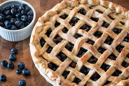 Homemade blueberry pie with lattice crust on a wooden background with loose blueberries