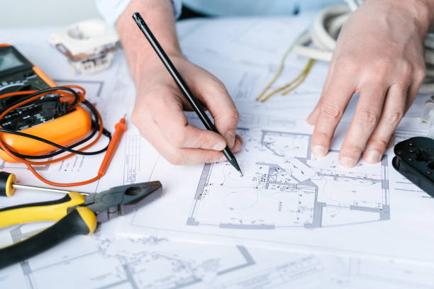 istock Man,repairer making electricity project in house.Repairs planning.Drawings,diagrams,plan for electrification of apartment,building.Devices,accessories,voltmeter,wires,screwdriver,pliers,tape measure 1418016914
