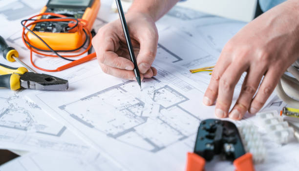 istock Man,repairer making electricity project in house.Repairs planning.Drawings,diagrams,plan for electrification of apartment,building.Devices,accessories,voltmeter,wires,screwdriver,pliers,tape measure 1418016922
