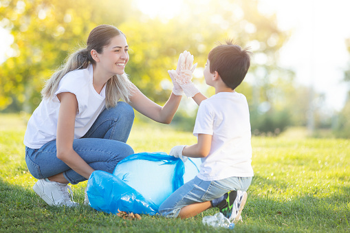 cute boy with his mother throws garbage in the garbage bag over the grass