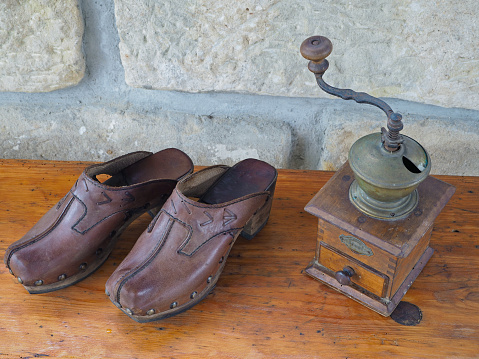 old antique hand coffee grinder and leather clogs on old wooden desk with sandsotone wall background