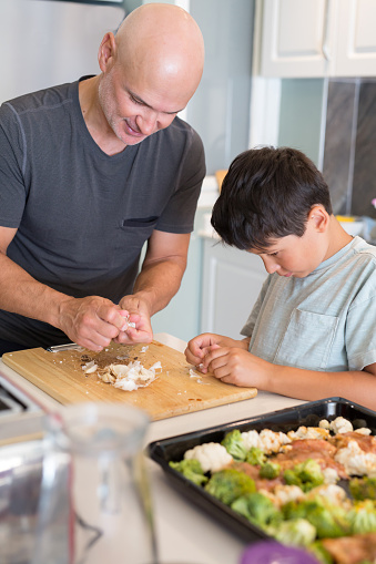 Father and son cut up garlic on a cutting board for their dish they are making together in the kitchen