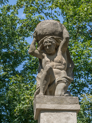 Stone men figure carrying stone, baroque statue from Greek mythology of Sisyphus or Sisyphos, garden, green trees background, czech republic