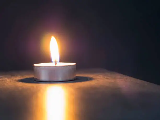 single tea light candle in the dark on the soft blurred grey background