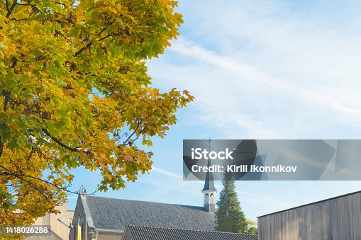 istock Autumn cityscape. A small church building in the city center. Fragment of the roof on an autumn background 1418026288