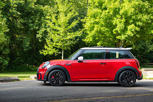 Toronto, Ontario, Canada- August 25, 2022. Chili red colour MINI COOPER on the road in public park in Toronto East side, Canada. This is the third generation model F56 JCW, since BMW took over iconic brand of MINI. MINI featured in the photo is John Cooper Works model, the most powerful 2 door version. For the first time, this compact car features engine build and designed by BMW, and packs even more power and torque than previous models since 2002 to present. Original design clues and themes are still present on this brand new model. Mini has been around since 1959 and has been owned and issued by various car manufacturers.