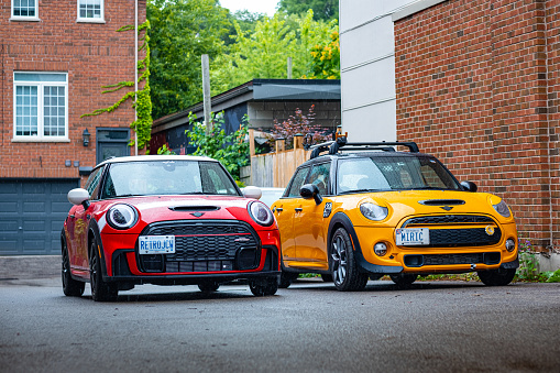 Toronto, Ontario, Canada- August 25, 2022. Pair of MINI COOPER cars on the urban street.  This is the third generation model F56 JCW, since BMW took over iconic brand of MINI. MINI featured in the photo is John Cooper Works model, the most powerful 2 door version. For the first time, this compact car features engine build and designed by BMW, and packs even more power and torque than previous models since 2002 to present. Original design clues and themes are still present on this brand new model. Mini has been around since 1959 and has been owned and issued by various car manufacturers.