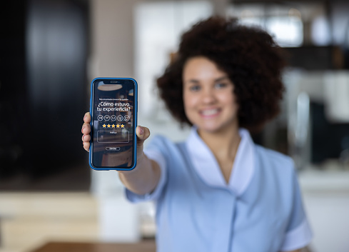 Latin American cleaner displaying an app to rate your experience after she has cleaned you house - mobile app service concepts