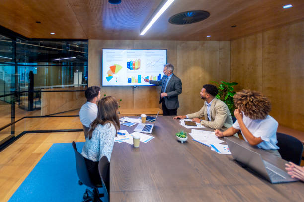 istock Mature man giving a big data presentation on a tv in a board room. 1418039080
