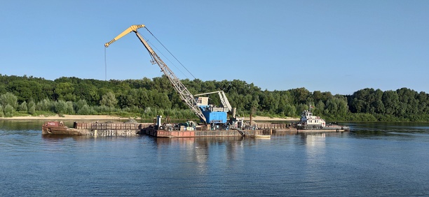 A barge loading sand into a large barge on the river transports cargo by water.