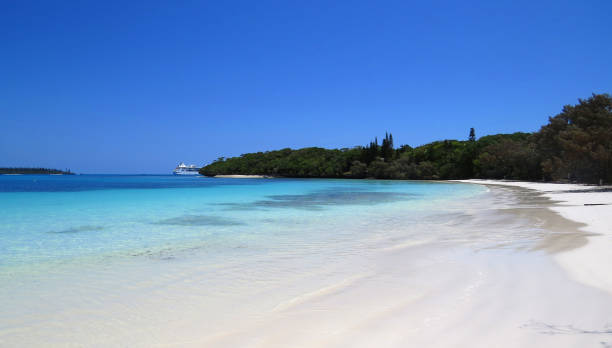 Turquoise water white sandy beach with a cruise ship docking on the background in Isle of Pines, New Caledonia. stock photo