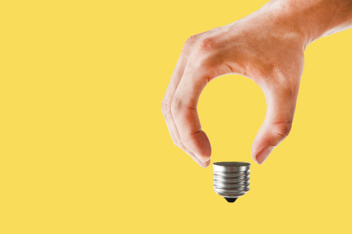 Abstract conceptual image of a hand holding light bulb on yellow background