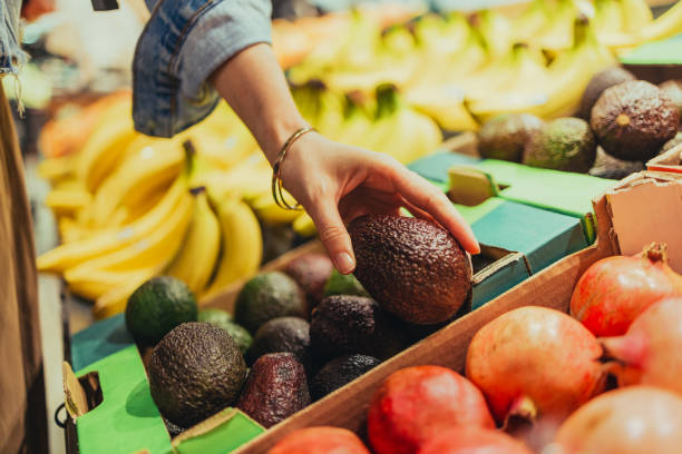 mujer anónima eligiendo aguacates en el supermercado - granada fruta tropical fotografías e imágenes de stock