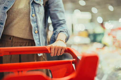 Cropped photo of an anonymous woman pushing a red shopping cart. She is wearing a blue denim jacket.