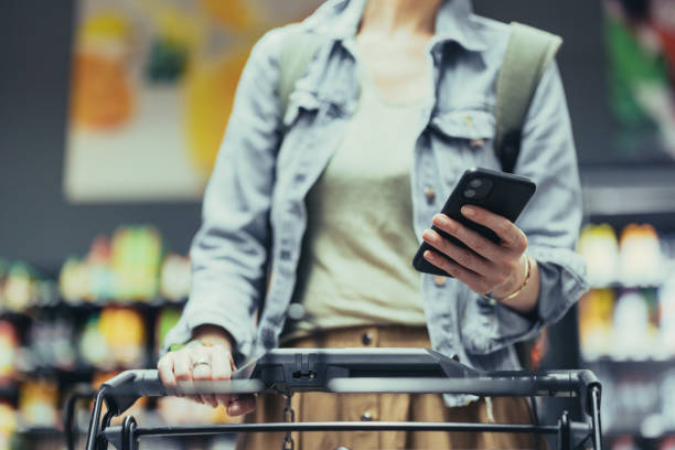 istock Anonymous Woman Texting on her Smartphone While Pushing Shopping Cart Down the Isle 1418045469
