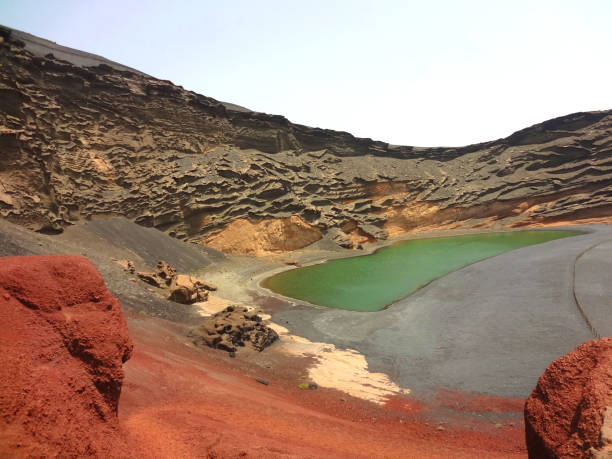 Mysterious bright green coloured lagoon lake nestled within the black sand, lava rock and red rock formations on the volcanic island of Lanzarote, Canary Islands. stock photo