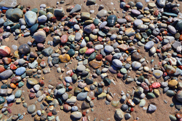 Plenty of colourful, beautiful, different sized wet stones lying on the sandy beach stock photo