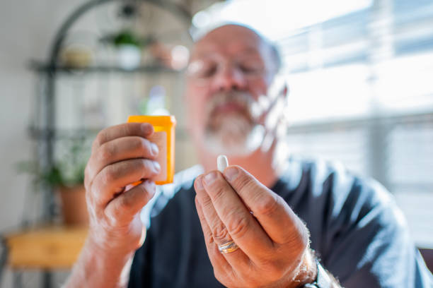Mature Man Scrutinizing His Perscription Medications Holding a Pill in One Hand and the Bottle in the Other In a Modern Home stock photo