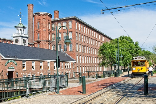 Lowell MA, USA — ,July 10, 2014: Boott Cotton Mill with trolley in front at Lowell National Historical Park. The Park preserves the 19th Century Industrial Revolution era textile manufacturing.