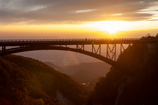 A lone person stands on a high bridge in the mountains of Fukushima Prefecture watching the sunrise.